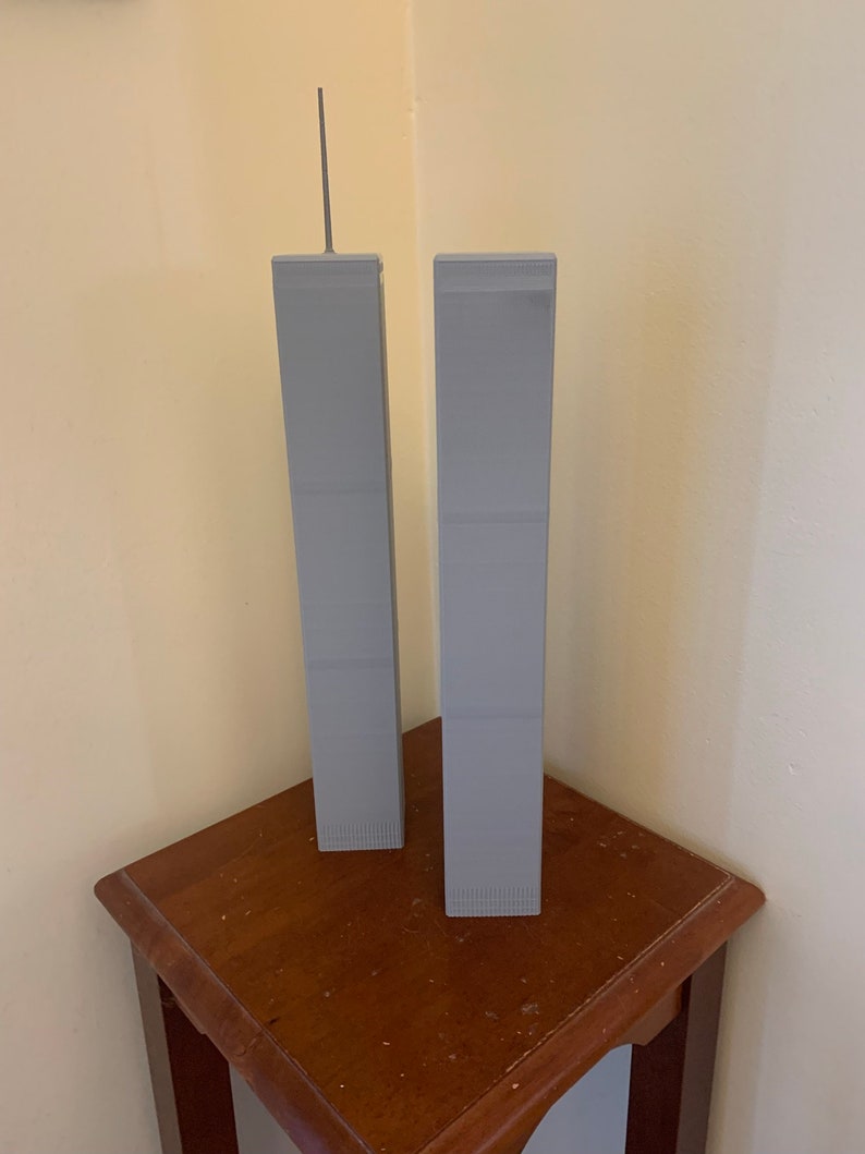 May include: Two grey miniature models of the World Trade Center towers on a wooden table.