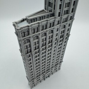 May include: A grey, three-dimensional model of a building with a distinctive triangular shape. The model features numerous windows and architectural details, and it is a miniature replica of a famous skyscraper.