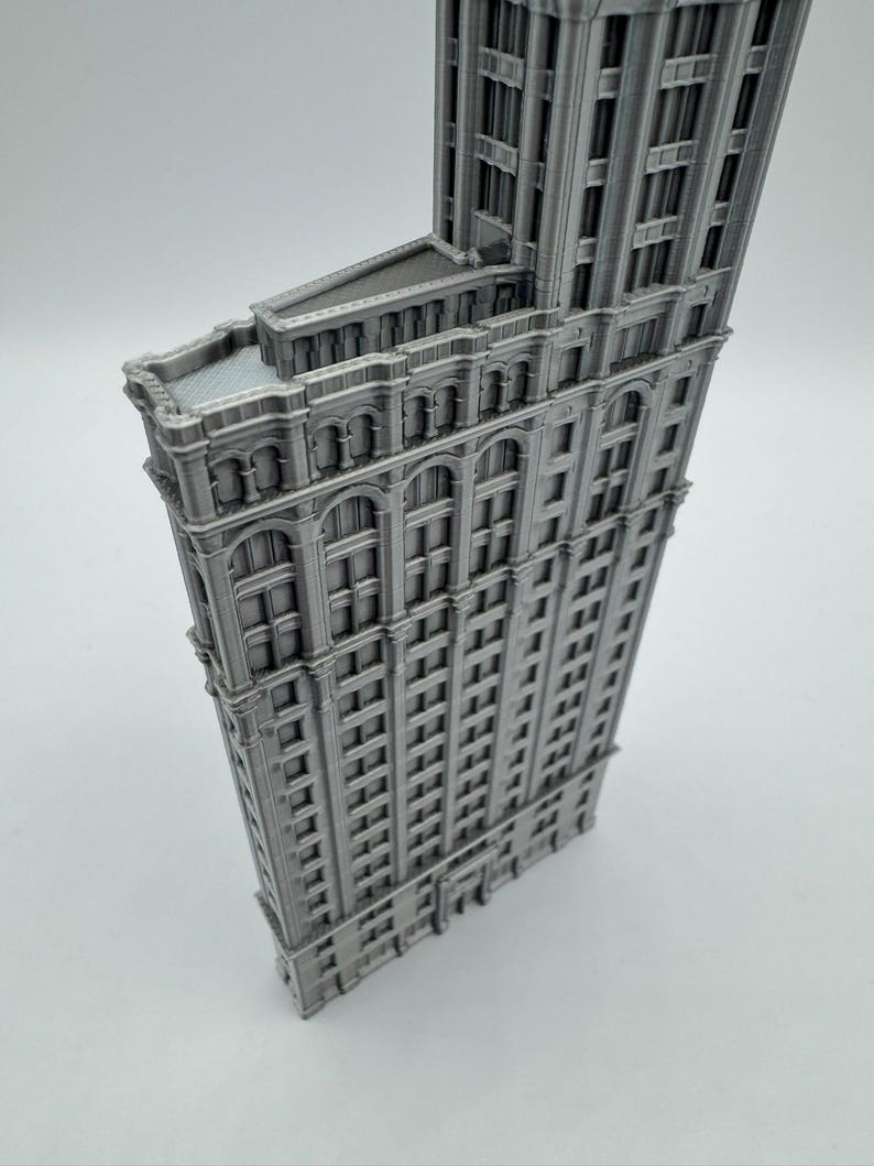 May include: A grey, three-dimensional model of a building with a distinctive triangular shape. The model features numerous windows and architectural details, and it is a miniature replica of a famous skyscraper.