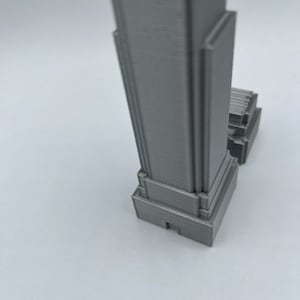 May include: A gray 3D printed model of a skyscraper.