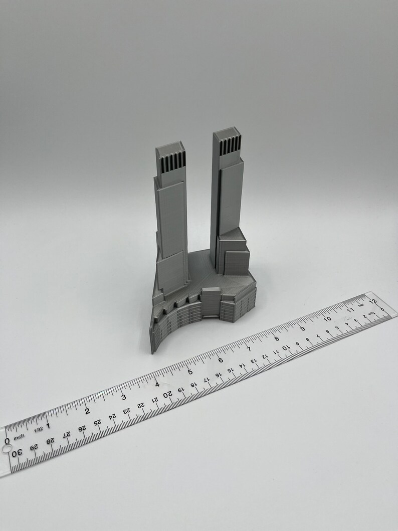 Op de afbeelding: Een 3D-geprint model van een paar wolkenkrabbers met een gebogen basis. Het model is gemaakt van grijs plastic en is ongeveer 10 cm hoog.