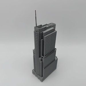 Może przedstawiać: Szary, miniaturowy model wieżowca z misternymi detalami architektonicznymi. Budynek ma prostokątną podstawę i wiele poziomów, z wysoką anteną na szczycie. Model wykonany jest z jednolitego, szarego materiału i na gładkim tle.