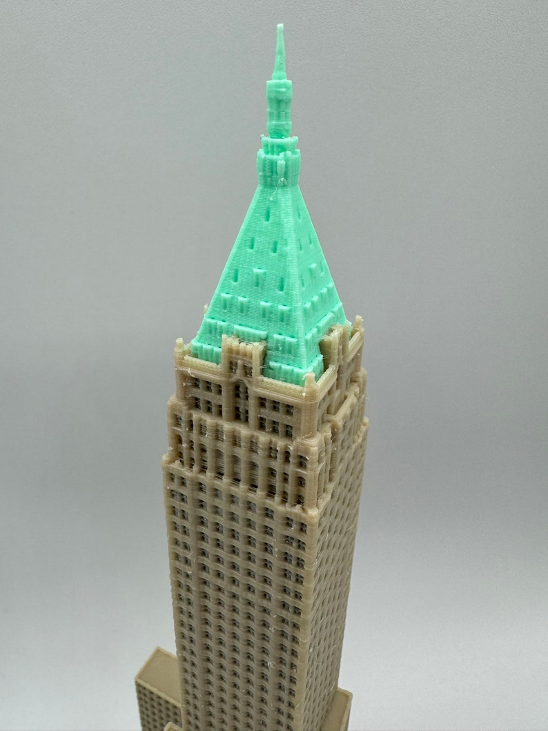 May include: A 3D printed model of a tall building with a green roof and a pointed spire. The building is made of a light brown plastic and has many windows.