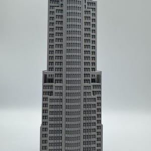 May include: A gray, detailed model of a skyscraper with numerous windows and a stepped design. The building has a tall, slender profile, and the windows are arranged in a grid pattern. The model is set against a plain white background.
