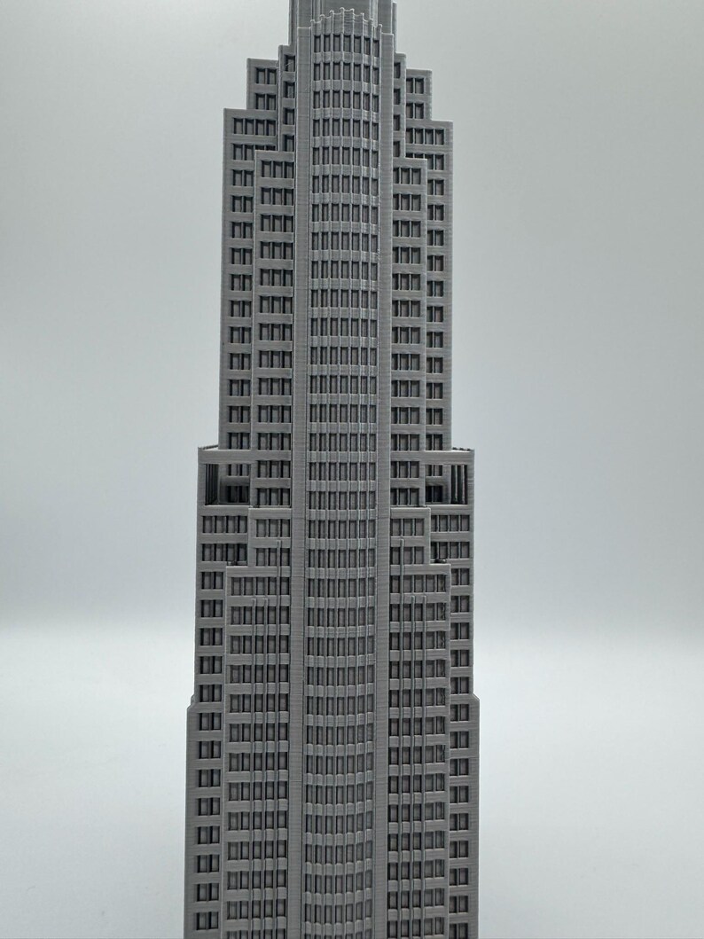 May include: A gray, detailed model of a skyscraper with numerous windows and a stepped design. The building has a tall, slender profile, and the windows are arranged in a grid pattern. The model is set against a plain white background.