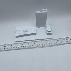 K&ouml;nnte beinhalten: Ein wei&szlig;es 3D-gedrucktes Modell eines Geb&auml;udes mit einer Kuppel auf dem Dach und einem Lineal im Vordergrund.