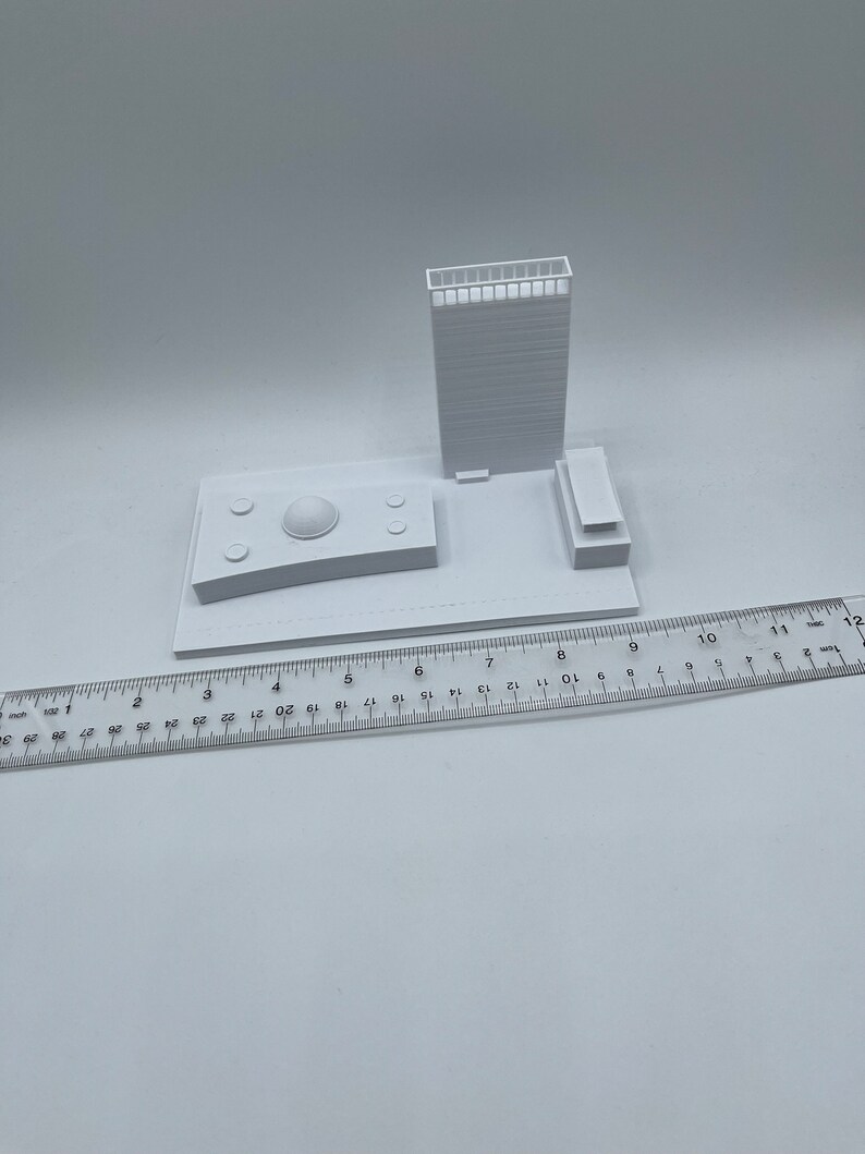 K&ouml;nnte beinhalten: Ein wei&szlig;es 3D-gedrucktes Modell eines Geb&auml;udes mit einer Kuppel auf dem Dach und einem Lineal im Vordergrund.