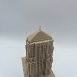 May include: A detailed miniature model of a tall, beige building with a pointed roof and many windows. The model is made of a smooth, light brown material.