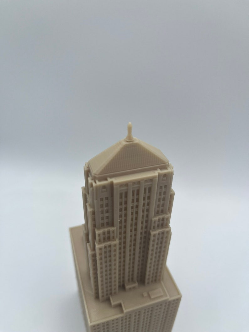 May include: A detailed miniature model of a tall, beige building with a pointed roof and many windows. The model is made of a smooth, light brown material.