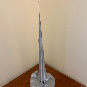 May include: A silver 3D printed model of the Burj Khalifa, the tallest building in the world, with a base that includes a detailed map of Dubai.