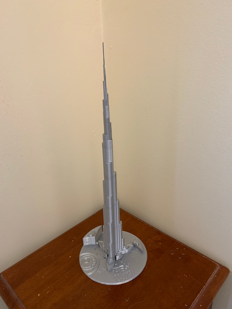 May include: A silver 3D printed model of the Burj Khalifa, the tallest building in the world, with a base that includes a detailed map of Dubai.