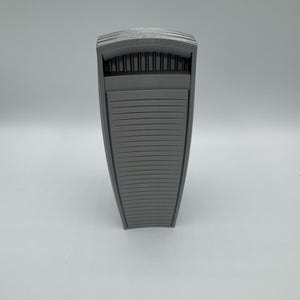 May include: A gray, architectural-style object with a rectangular shape and a slatted design on the front. The top features a series of vertical lines, and the overall appearance is modern and minimalist.