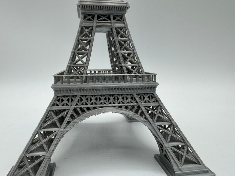 May include: A gray 3D printed model of the Eiffel Tower. The model is detailed and shows the intricate structure of the tower.