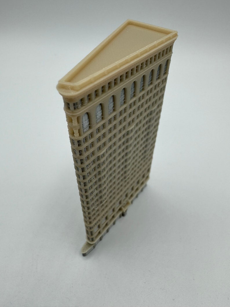 May include: A beige 3D printed model of the Flatiron Building in New York City. The model is detailed with windows and a triangular roof.