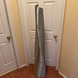 May include: A silver, metallic, twisted, cylindrical sculpture resembling a skyscraper.