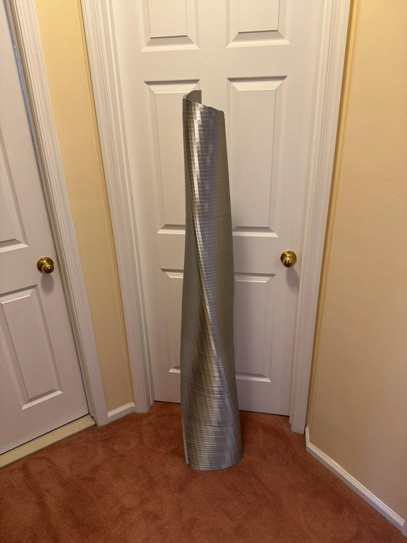 May include: A silver, metallic, twisted, cylindrical sculpture resembling a skyscraper.