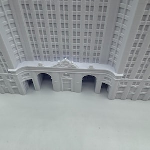 Puede incluir: Maqueta arquitect&oacute;nica blanca de un edificio con numerosas ventanas y entradas arqueadas. El modelo muestra detalles intrincados, incluyendo elementos decorativos sobre la entrada y a lo largo de la fachada. El dise&ntilde;o del edificio sugiere un estilo cl&aacute;sico e hist&oacute;rico.