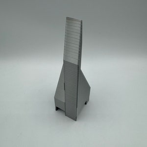 May include: A gray 3D printed model of a tall, slender building with a pointed roof and a rectangular base.