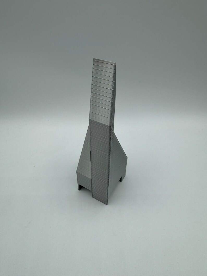 May include: A gray 3D printed model of a tall, slender building with a pointed roof and a rectangular base.
