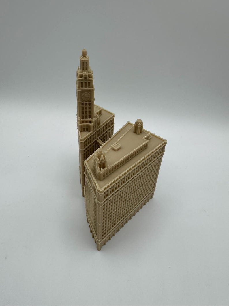 May include: Two beige miniature architectural models of buildings. One model features a tall clock tower, while the other is a rectangular building. Both models have detailed facades and are set against a white background.