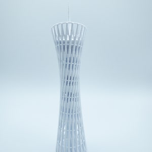 May include: White 3D printed model of a tall, slender tower with a lattice design. The tower has a pointed top and a circular base.