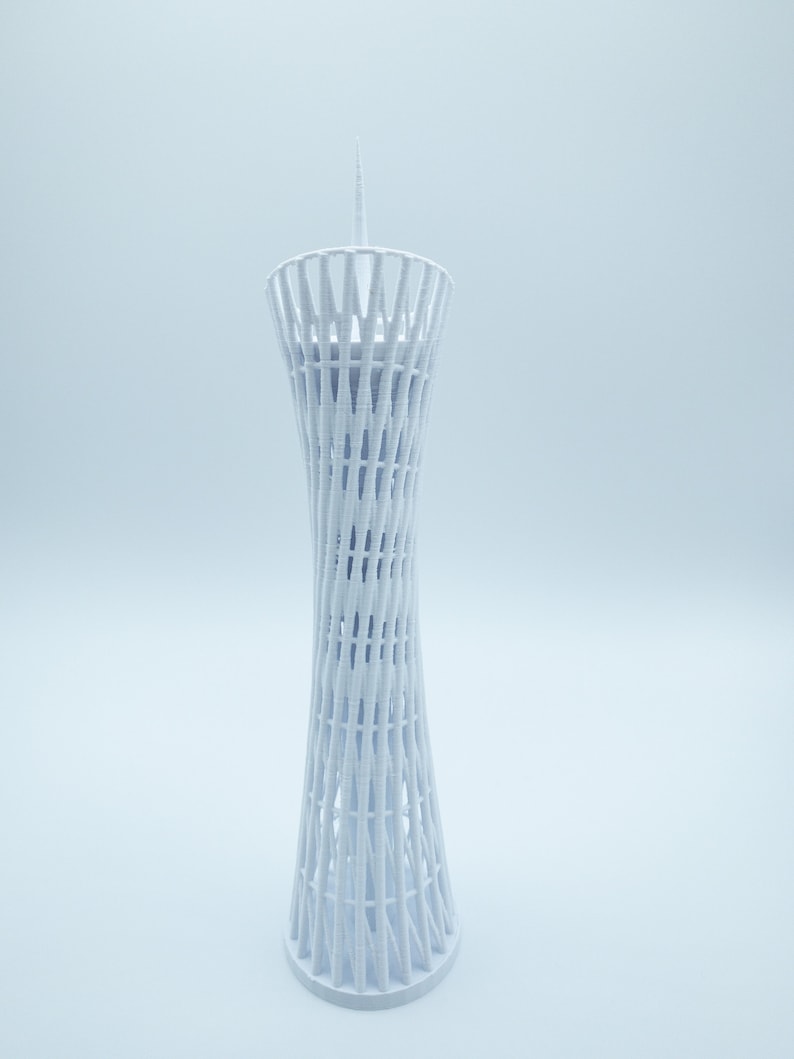 May include: White 3D printed model of a tall, slender tower with a lattice design. The tower has a pointed top and a circular base.