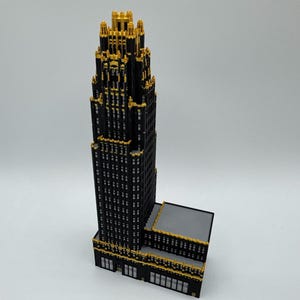 Peut inclure: Un modèle de gratte-ciel à plusieurs niveaux construit avec des briques de construction noires et dorées. La structure présente un design en gradins avec une tour centrale, des détails dorés complexes sur les bords et une base rectangulaire.