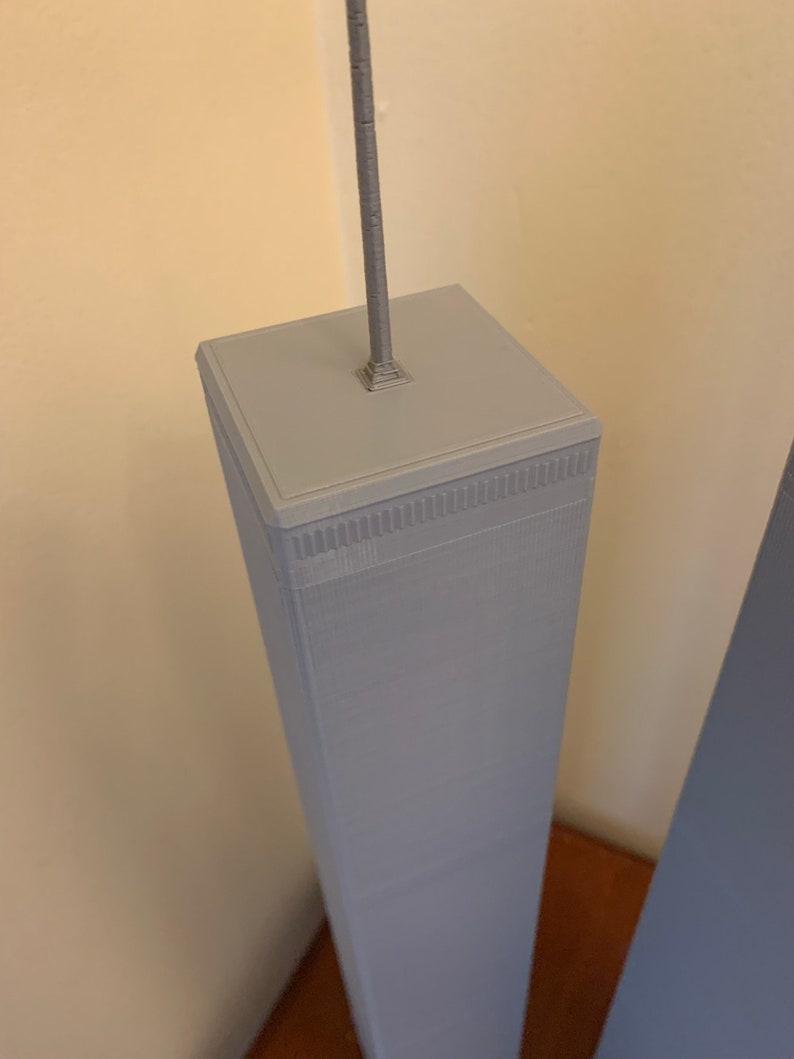 May include: A close-up of a grey 3D printed model of a skyscraper with a silver antenna on top.