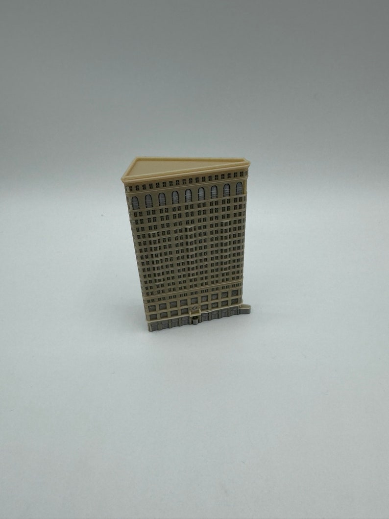 May include: A miniature model of a tall, beige building with many windows. The building has a triangular roof and a detailed facade.