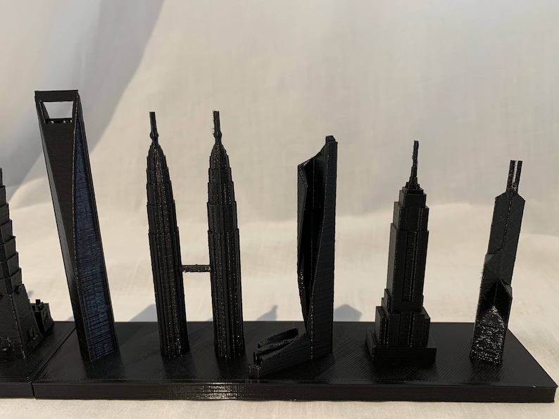 May include: A collection of black miniature skyscraper models, including the Shanghai World Financial Center, Petronas Towers, and the Empire State Building, mounted on a black base. The models are detailed and stand at varying heights.