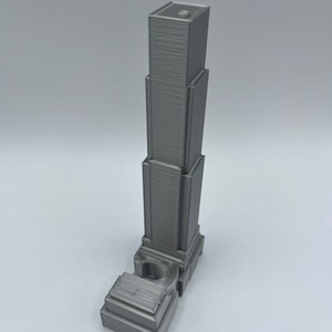 May include: A gray 3D printed model of a skyscraper with a detailed facade and a base.