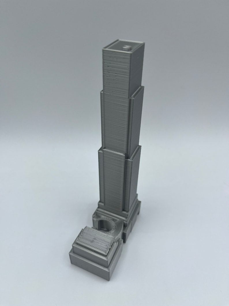 May include: A gray 3D printed model of a skyscraper with a detailed facade and a base.