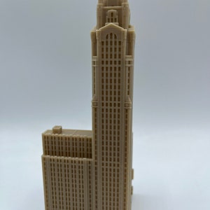May include: A beige 3D printed model of a tall skyscraper with a decorative top and many windows.
