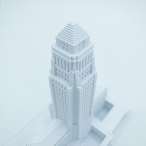 May include: A white 3D printed model of a tall building with a stepped roof. The model is detailed with windows and decorative elements.