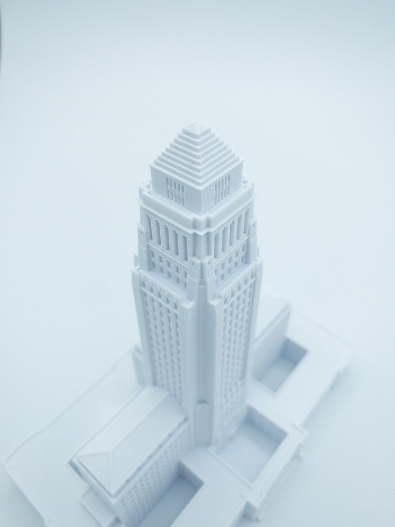 May include: A white 3D printed model of a tall building with a stepped roof. The model is detailed with windows and decorative elements.