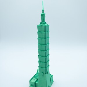 May include: A 3D printed model of a green skyscraper with a pointed top.