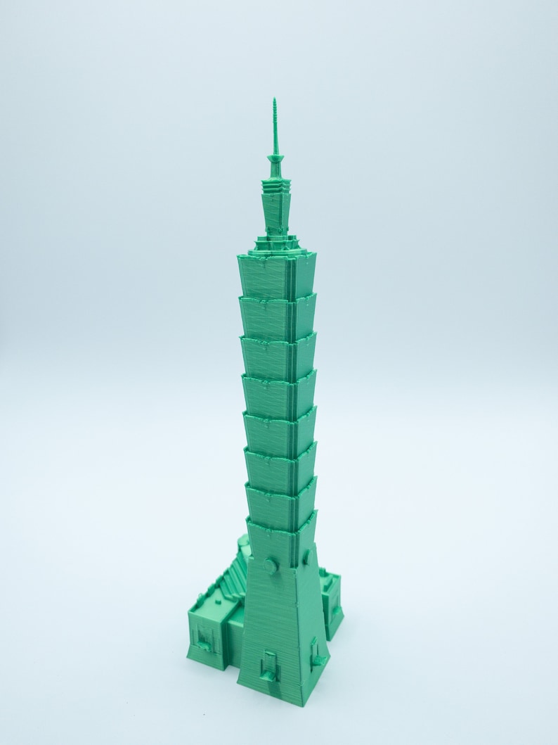 May include: A 3D printed model of a green skyscraper with a pointed top.