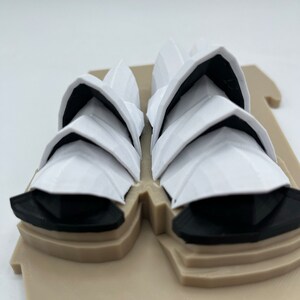 May include: A white 3D printed model of the Sydney Opera House. The model is on a tan base and has black details.