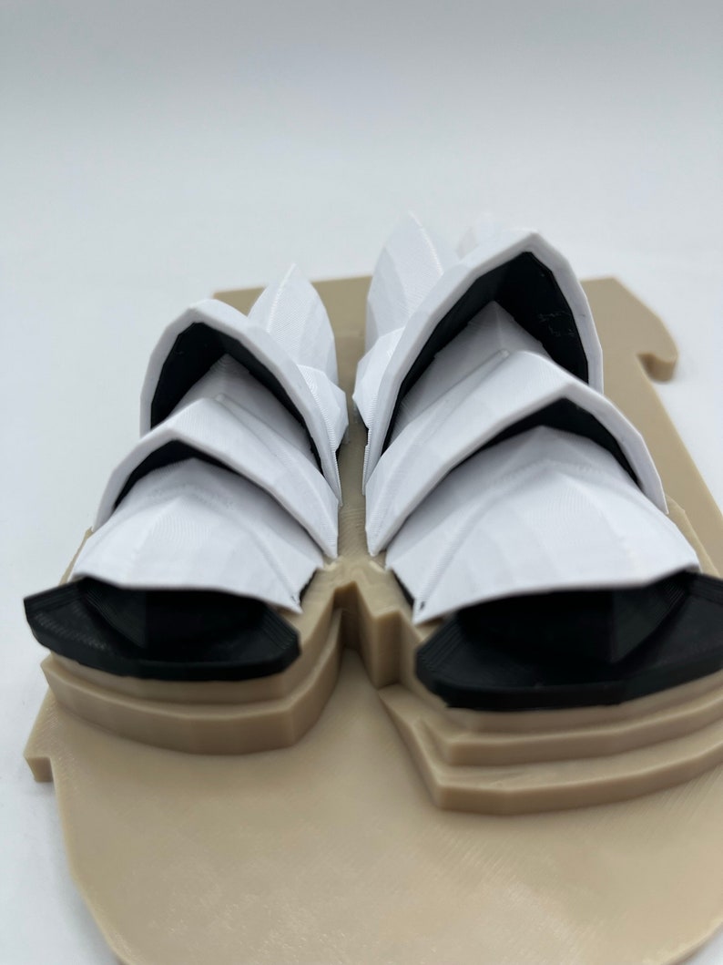 May include: A white 3D printed model of the Sydney Opera House. The model is on a tan base and has black details.