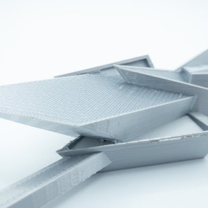 May include: A gray 3D printed model of a geometric shape with sharp angles and edges. The model is made of plastic and has a smooth, matte finish.