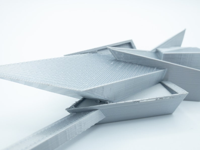 May include: A gray 3D printed model of a geometric shape with sharp angles and edges. The model is made of plastic and has a smooth, matte finish.