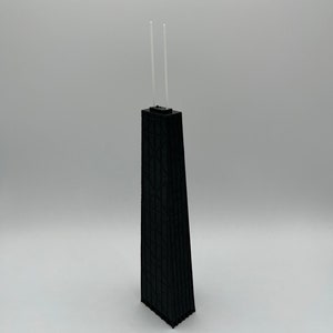 May include: A black architectural model of a skyscraper with two clear, vertical antennas. The building has a geometric facade and a rectangular base. The model is set against a plain white background.