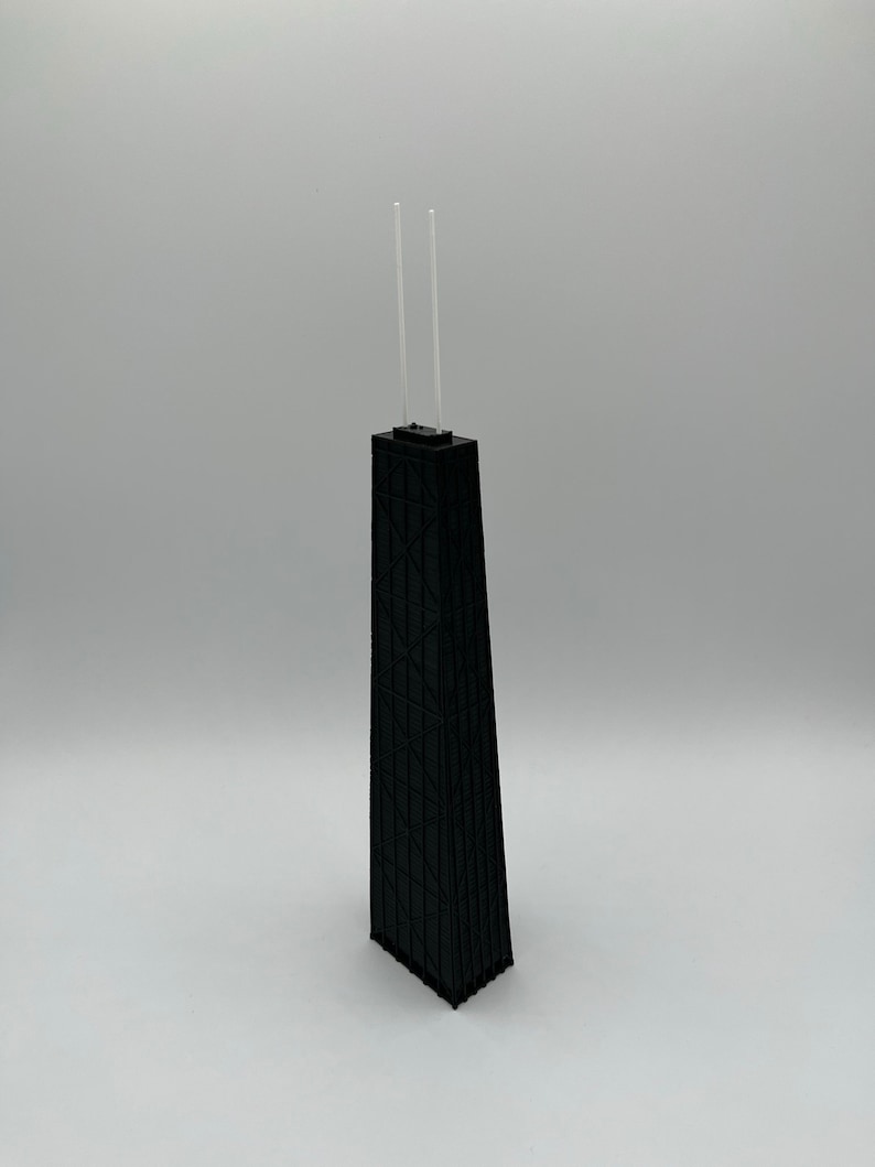 May include: A black architectural model of a skyscraper with two clear, vertical antennas. The building has a geometric facade and a rectangular base. The model is set against a plain white background.