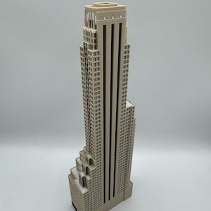 May include: A beige architectural model of a skyscraper. The building has a stepped design with multiple levels and a flat roof. The model is made of a light-colored material and stands tall against a plain background.