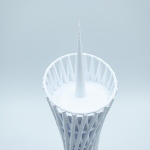 May include: White 3D printed model of a tower with a pointed top and a circular base.