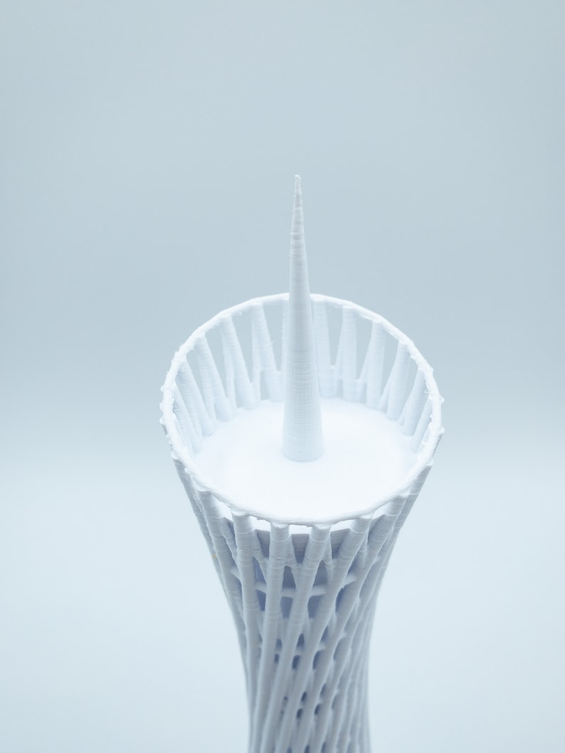 May include: White 3D printed model of a tower with a pointed top and a circular base.