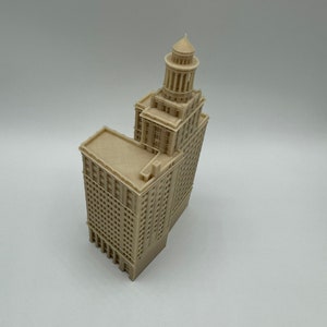 May include: A beige 3D printed model of a tall building with a domed roof. The building has many windows and a detailed facade.