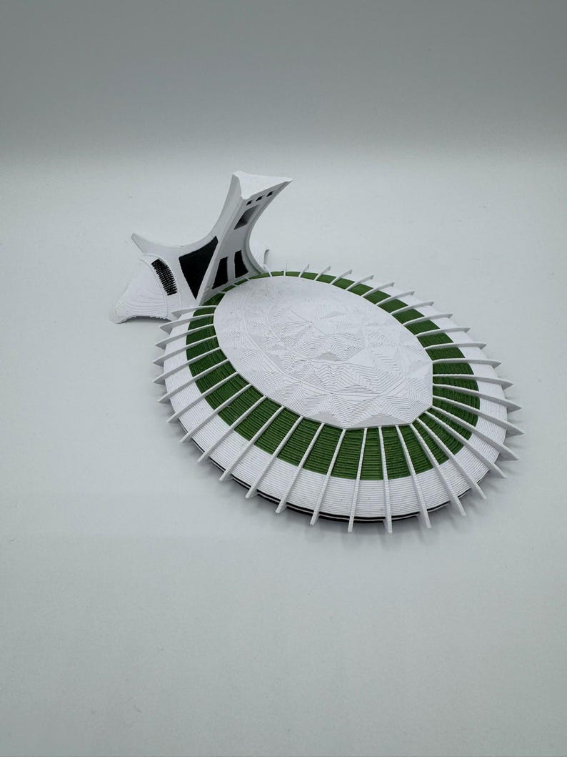 Puede incluir: Maqueta arquitect&oacute;nica blanca y verde con un dise&ntilde;o circular detallado. El modelo presenta una superficie central blanca texturizada rodeada de bandas verdes y blancas, y una estructura de soporte estilizada.