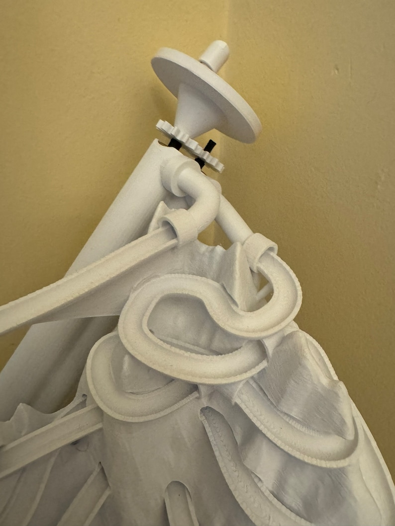 May include: White 3D printed sculpture of a person with a large hat and a complex, winding track system. The track system is made of white plastic and appears to be a marble run.
