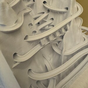 May include: White 3D printed sculpture with a complex, intricate design of interconnected curves and loops.